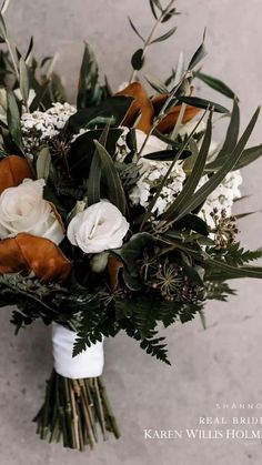 a bridal bouquet with white and brown flowers on the side, in front of a gray wall