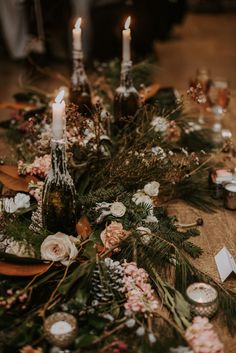 a table topped with candles and flowers next to bottles of wine on top of a wooden table