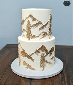 a three tiered cake with mountains and pine trees on the top is decorated with gold foil