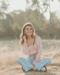 a woman sitting on the ground with her hands in her pockets and smiling at the camera