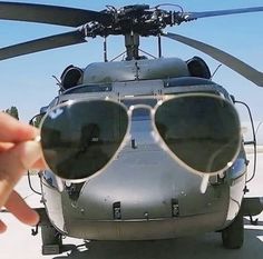 a hand holding up a pair of sunglasses in front of a helicopter