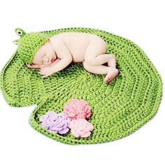 a baby sleeping on top of a green mat with crocheted flowers around it