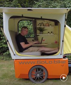 a man sitting in the back of an orange and white truck with a laptop on it