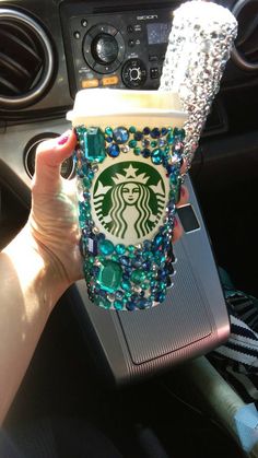 a person holding up a starbucks cup in their hand with beads and jewels on it