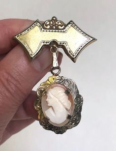 "Vintage Brooch Cameo Victorian Carved Shell Dangle Pin This beautiful victorian revival brooch is most likely from the 1940s and his a wonderful true victorian design! This pieces starts with a double arrow shaped brooch with a bit of victorian scroll on the top. Suspending by an etched bale is the most lovely genuine carved shell cameo of a women in profile in an ivory color on a peach colored shell oval. the cameo is set with four prongs and surrounded by a stunning scalloped oval gold frame Bijoux Art Nouveau, Jewelry Casket, Victorian Revival, Vintage Jewelry Sets, Cameo Jewelry, Victorian Lace, Victorian Design, Beaded Rope, Art Nouveau Jewelry