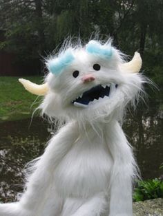 a white furry monster with blue eyes and long hair sitting on top of a rock