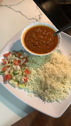 a white plate topped with rice and beans next to a bowl of chili sauce on top of it