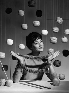 a woman sitting at a table with balls of yarn hanging from the ceiling