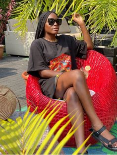 a woman sitting in a red chair with sunglasses on her head and palm trees behind her