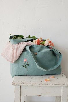 a blue bag sitting on top of a wooden table next to a white chair and flowers