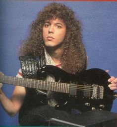 a man with long hair is holding a guitar and posing for the camera while wearing a leather vest