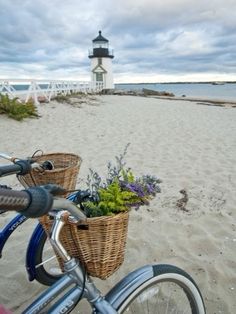 a bicycle parked on top of a sandy beach next to the ocean with a light house in the background