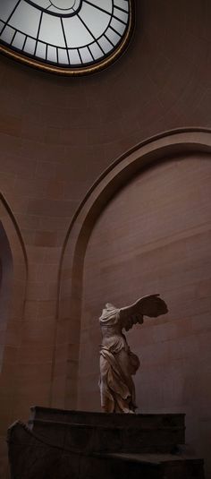 an angel statue in the middle of a room with a round window above it and a clock on the wall