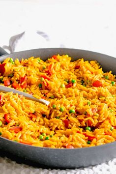 a pan filled with rice and peas on top of a white cloth next to a spoon