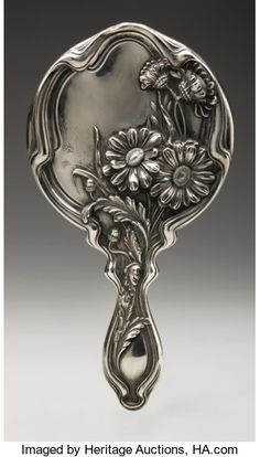 an ornate silver plate with flowers and leaves on the handle is shown in front of a gray background