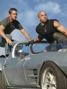 two men are standing on the hood of a sports car and one is leaning over