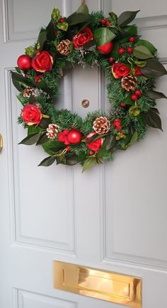 a christmas wreath hanging on the front door with pomegranates and pine cones