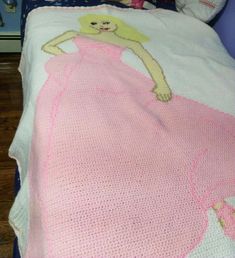 a child's bed with a crocheted pink dress and teddy bear on it