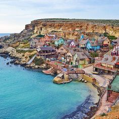 an aerial view of a small town on the coast with blue water and cliffs in the background