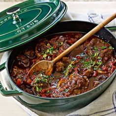 a green pot filled with stew and a wooden spoon on top of a white cloth