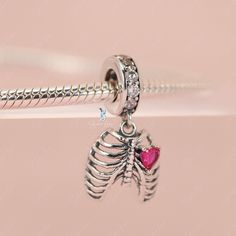 This is charm only, bracelet is sold separately. Experience true love with this exquisite pendant charm featuring a silver rib cage adorned with a stunning pink heart stone. Made of high-quality 925 sterling silver, its polished finish adds a brilliant shine and is accented with a platinum plating. Add this beautiful love oath of rib dangle pendant charm to your bracelet or gift it to your special someone. Materials: 925 sterling silver, cubic zirconiaFinish: platinum plateDimensions: 0.76 x 0.4 Silver Heart Pendant Jewelry In Stainless Steel, Silver Stainless Steel Heart Pendant Jewelry, Pink Sterling Silver Dangle Charms, Elegant Sterling Silver Pendant Charms, Pink Sterling Silver Charm Necklace With Heart Charm, Nickel Free Open Heart Stainless Steel Jewelry, Pink Sterling Silver Necklace With Heart Charm, Nickel-free Open Heart Stainless Steel Jewelry, Nickel-free Stainless Steel Open Heart Jewelry