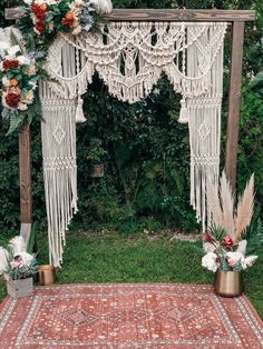 an outdoor wedding ceremony setup with macrame and flowers on the rug, potted plants in gold vases