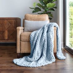 a chair with a blanket on top of it next to a potted plant in front of a window