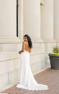 a woman in a white dress standing on the side of a building with her back to the camera