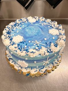 a blue and white frosted cake with snowflakes on the top is sitting on a silver surface