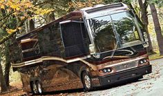 a motor home parked on the side of a road in front of trees with fall leaves