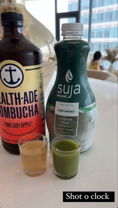 two bottles of juice sitting on top of a table next to a shot glass filled with liquid