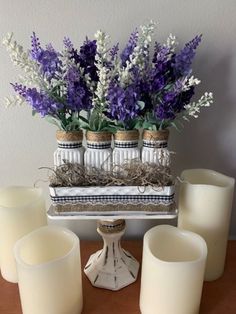 there are candles and vases on the table with purple flowers in each candle holder