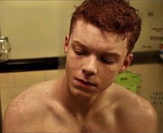 a shirtless young man is looking at his cell phone in the bathroom with water all over his face