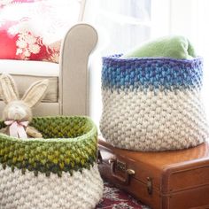 two knitted baskets sitting next to each other on top of a rug in front of a chair