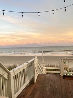 a wooden deck overlooking the beach with string lights strung over it and an ocean in the background