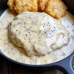 some food is in a black pan on a wooden table and it looks like cheese sauce