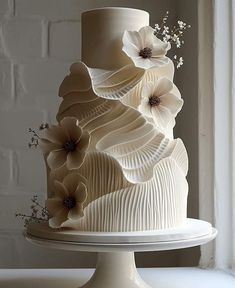 a three tiered cake with white icing and flowers on the top, sitting on a pedestal