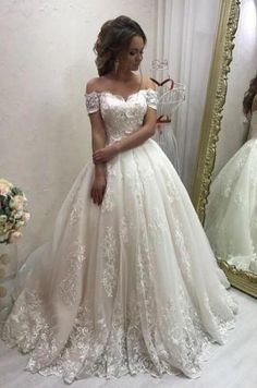 a woman standing in front of a mirror wearing a wedding dress with off the shoulder sleeves