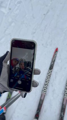 someone is holding up their cell phone to take a selfie with skis in the background