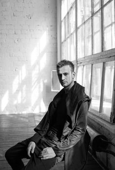 a man sitting in front of a window next to a brick wall and wooden floor