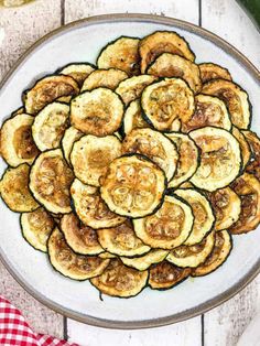 a white plate topped with sliced zucchini on top of a table next to a red and white checkered napkin