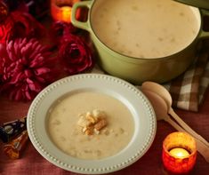 a bowl of soup next to a candle and some other items on a table with flowers