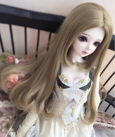 a doll with long blonde hair sitting on a bed