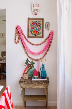 there is a table with flowers and vases on it next to a wall hanging