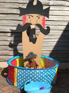 a cardboard cutout of a pirate in a blue pail filled with sand and toys