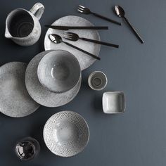 an assortment of dishes and utensils are arranged on a gray tablecloth with silverware