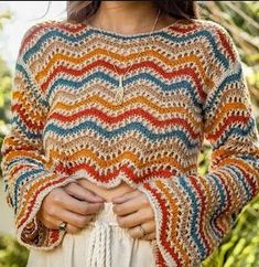 a woman wearing a multicolored crochet sweater with her hands in her pockets