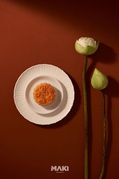 a white plate with food on it next to a single flower and a red wall