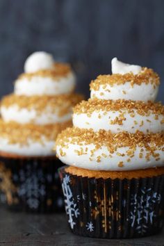 three cupcakes with white frosting and gold sprinkles on top