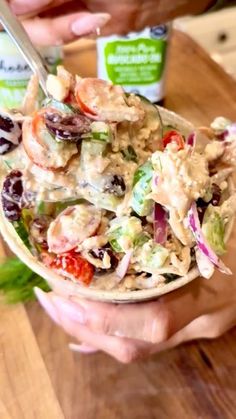 two hands holding a bowl of salad with shrimp and lettuce in it on a wooden table